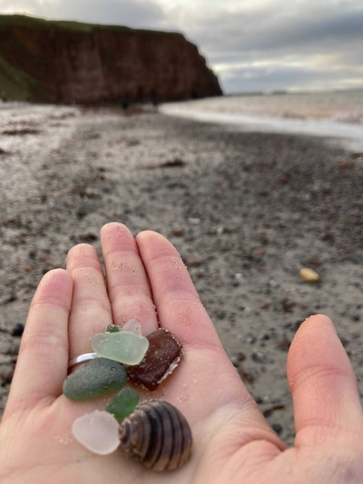 Sea-glass and a shell in my hand, with the beach in the background