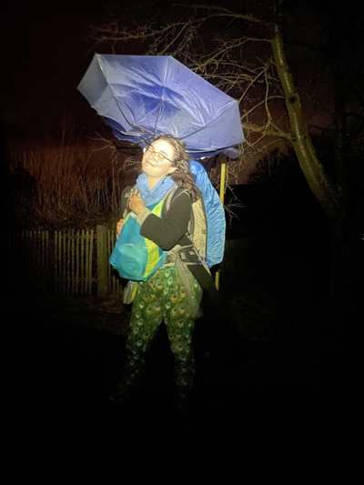 A nighttime picture of me in my peacock leggings with an inside-out umbrella and two backpacks on