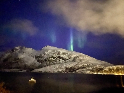 northern lights over a mountain with a boat in the fjord in front of it