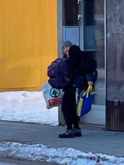 Maggie carrying 2 backpacks, a giant coat and two tote bags